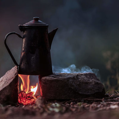 A tea kettle on a camp fire.