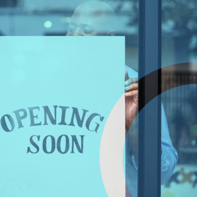 Man hangs an "Opening Soon" sign at the front of his small business window.