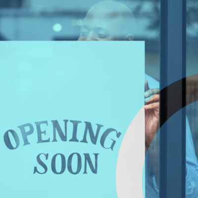 Man hangs an "Opening Soon" sign at the front of his small business window.