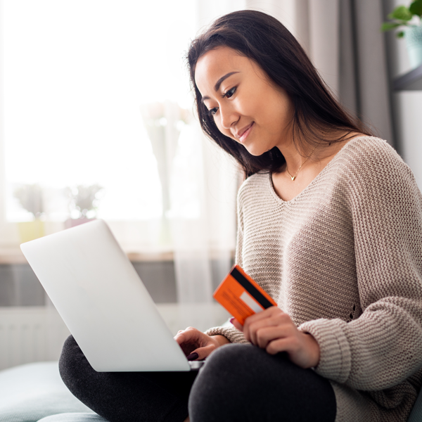 Woman with credit card sitting on a couch with a laptop