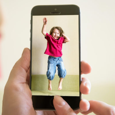 Mother taking photo of jumping baby girl with her mobile phone
