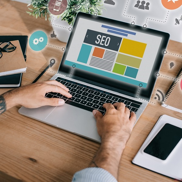 cropped shot of developer using laptop with SEO icons at workplace