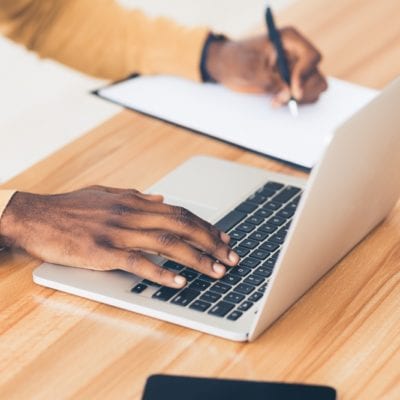 Unrecognizable black guy working on his laptop and writing