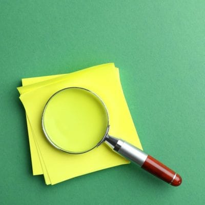 Magnifier glass and empty paper sheets on green background, flat lay with space for text. Find keywords concept