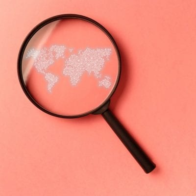 Concept information search. Magnifying glass with international map on coral background.