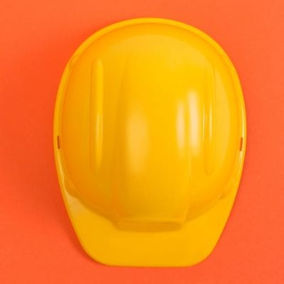 Yellow construction helmet on an orange background, protection and safety concept