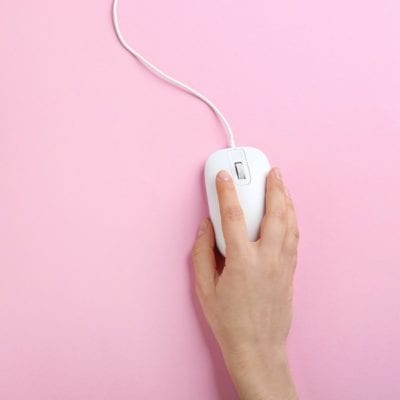 Woman using modern wired optical mouse on pink background, top view.