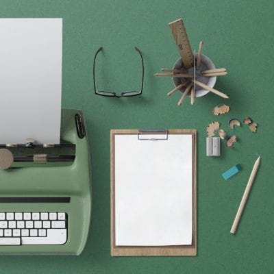 typewriter, notepad, glasses, and pencils behind a dark forest green background