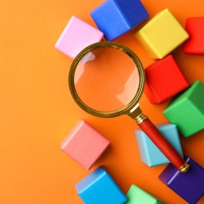 Magnifying glass on an orange background, surrounded by multi-colored blocks. Finding what you need in a Google Product Search.