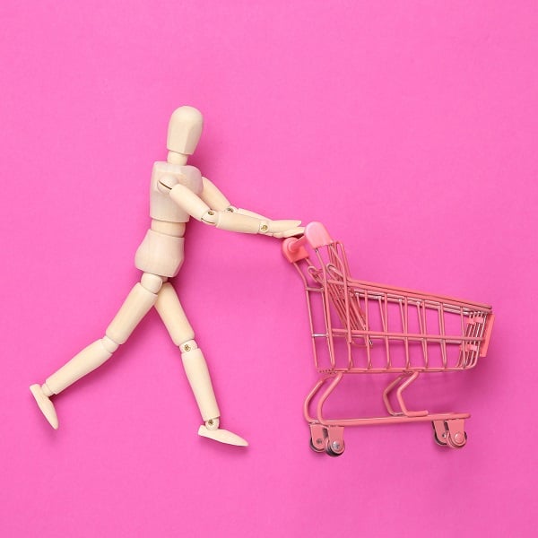 Wooden puppet with Mini shopping cart on pink background