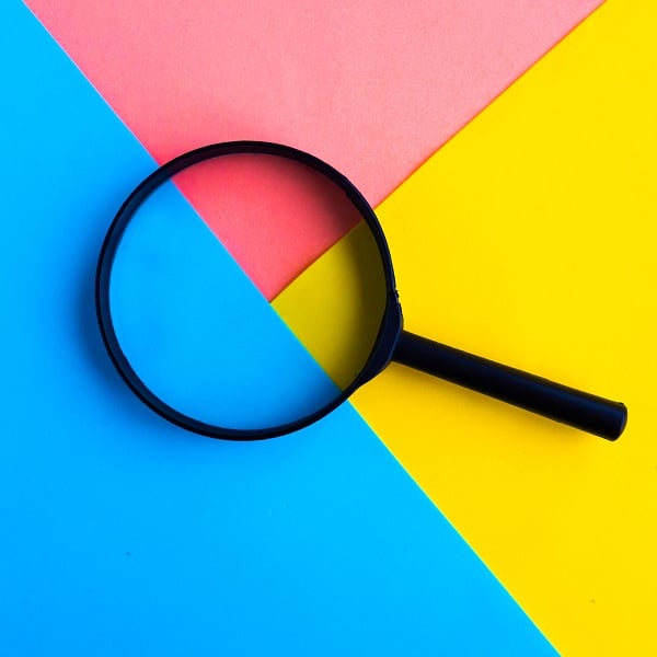 Magnifying glass on bright geometric pink, blue and yellow background. Minimal concept