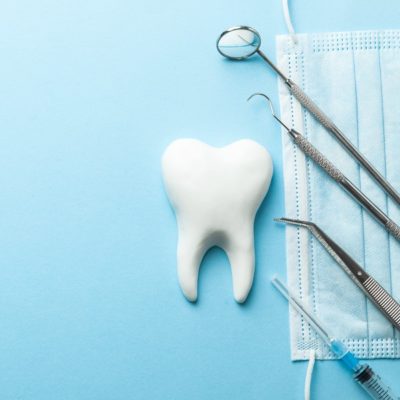 Tooth and dental instruments on blue background. Dental treatment. Dentist tools mirror, hook, tweezers, syringe. Copy space for text.