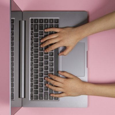 Kid hands typing on laptop computer keyboard, top view, pink banner background