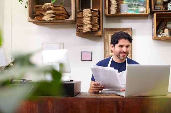 Male Assistant Working On Laptop Behind Sales Desk Of Florists Store