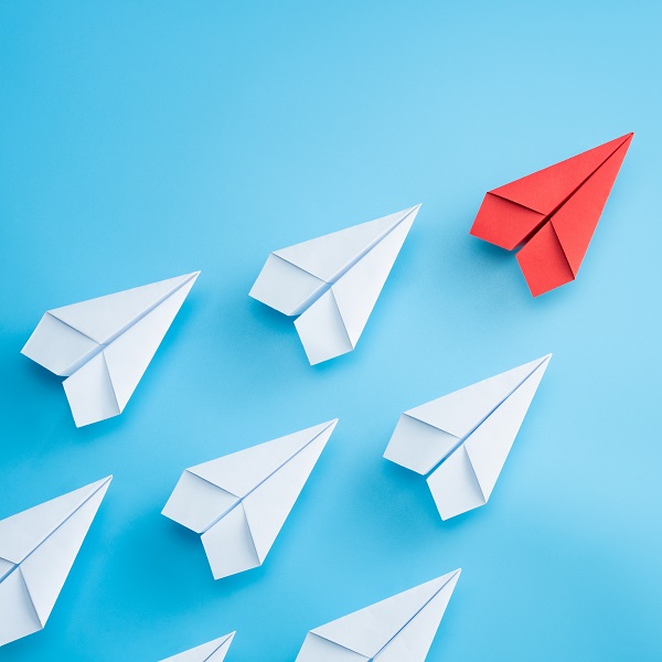 Leadership concept with red paper plane leading among white on blue background