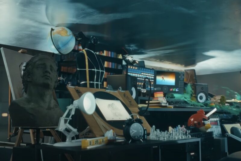 A wide variety of creative tools, including a piano, cameras, paint, and a bust, sit on a platform before being crushed by a hydraulic press in an Apple advertisement.